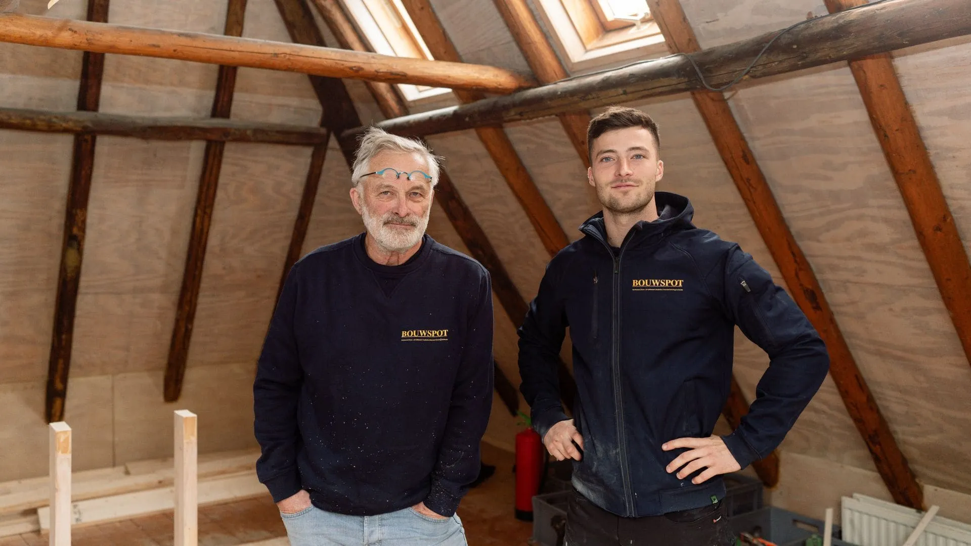 Merik Sliedrecht en zijn vader Rens in Bouwspot-werkkleding op een zolder met houten kapconstructie